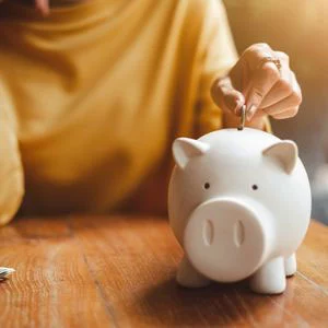 person inserting coin into piggy bank